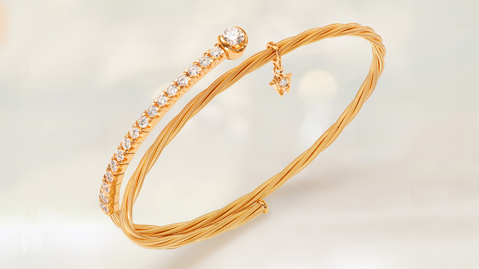 Das Armband UMARME MICH Power of diamonds aus 18-karätigem federnden Gelbgold und funkelnden, handgefassten Brillanten. Auf grauem Mood Hintergrund.