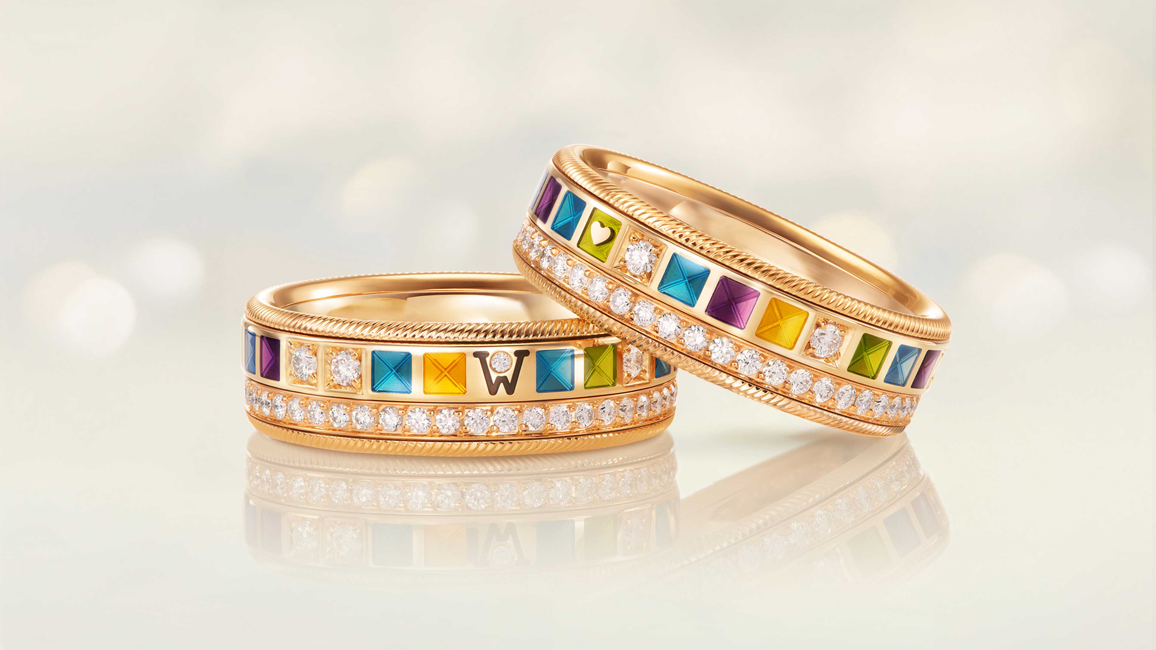 Der Ring POWER IN COLOUR aus 18 Karat Gelbgold fasziniert mit neunfarbiger Kaltemaille, grünem Herz und Brillanten, drehbar auf hellem Hintergrund.