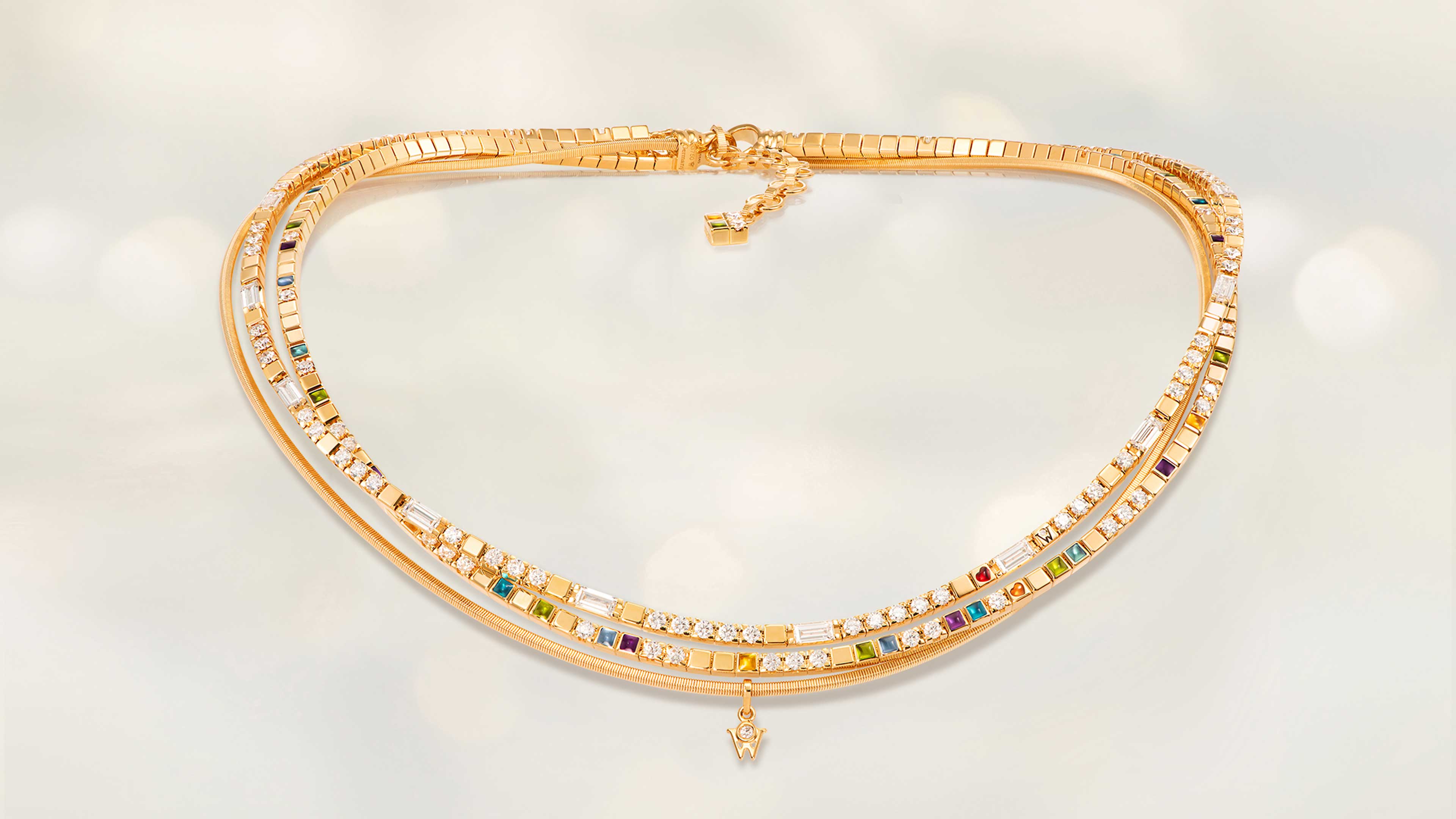 Das Collier POWER IN COLOUR edel aus 18 Karat Gelbgold fasziniert mit Kaltemaille in neun Farben, Brillant-Baguettestrang und orangefarbenem Herz. Collier auf hellem Hintergrund.