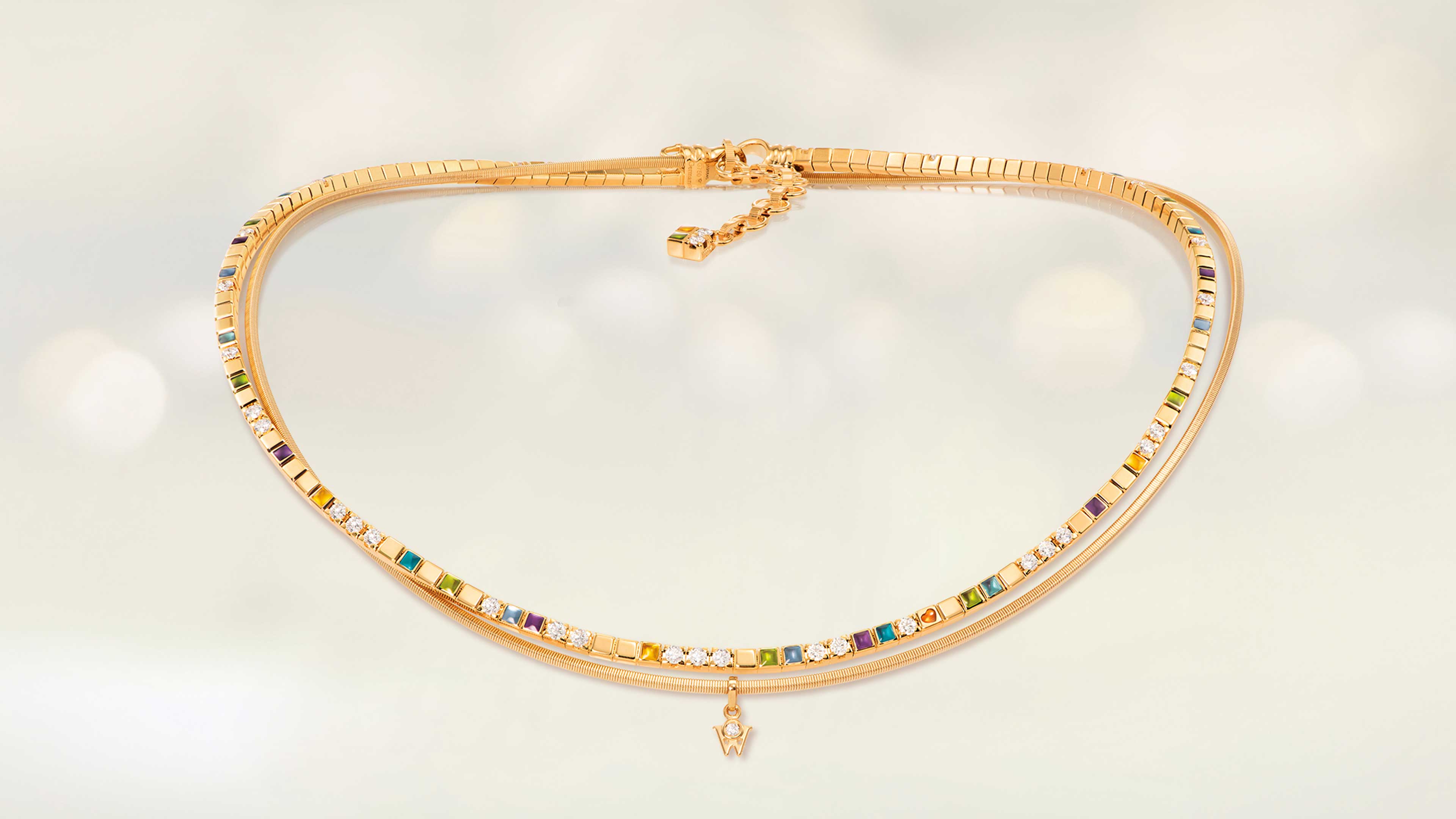 Das Collier POWER IN COLOUR aus 18 Karat Gelbgold begeistert mit Kaltemaille in acht Farben und einem kleinen orangefarbenen Herz. Collier auf hellem Hintergrund.