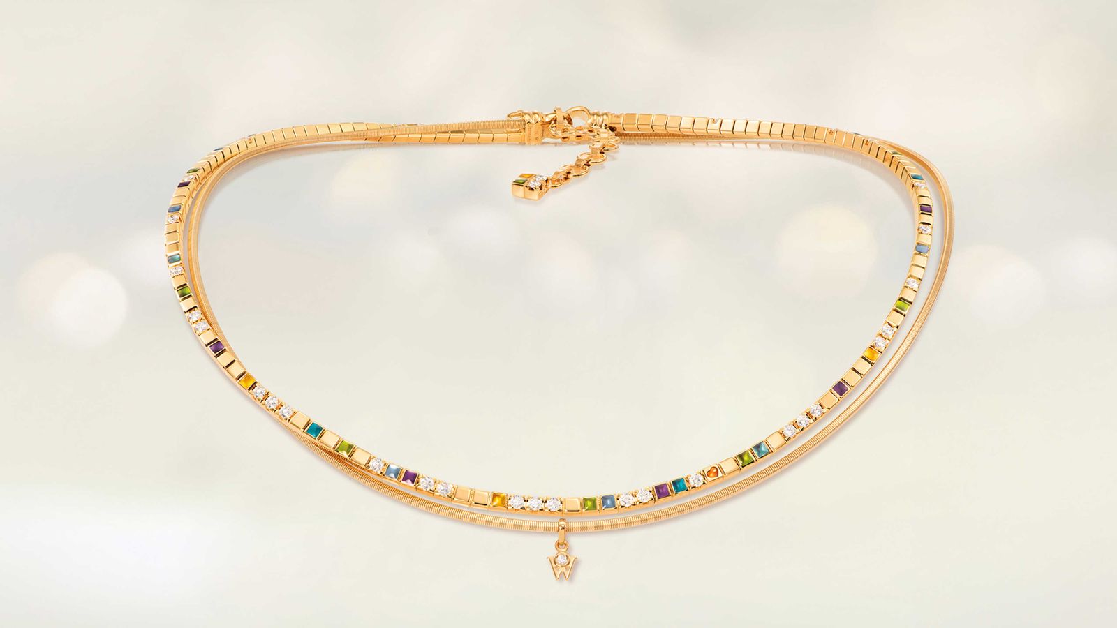 Das Collier POWER IN COLOUR aus 18 Karat Gelbgold begeistert mit Kaltemaille in acht Farben und einem kleinen orangefarbenen Herz. Collier auf hellem Hintergrund.