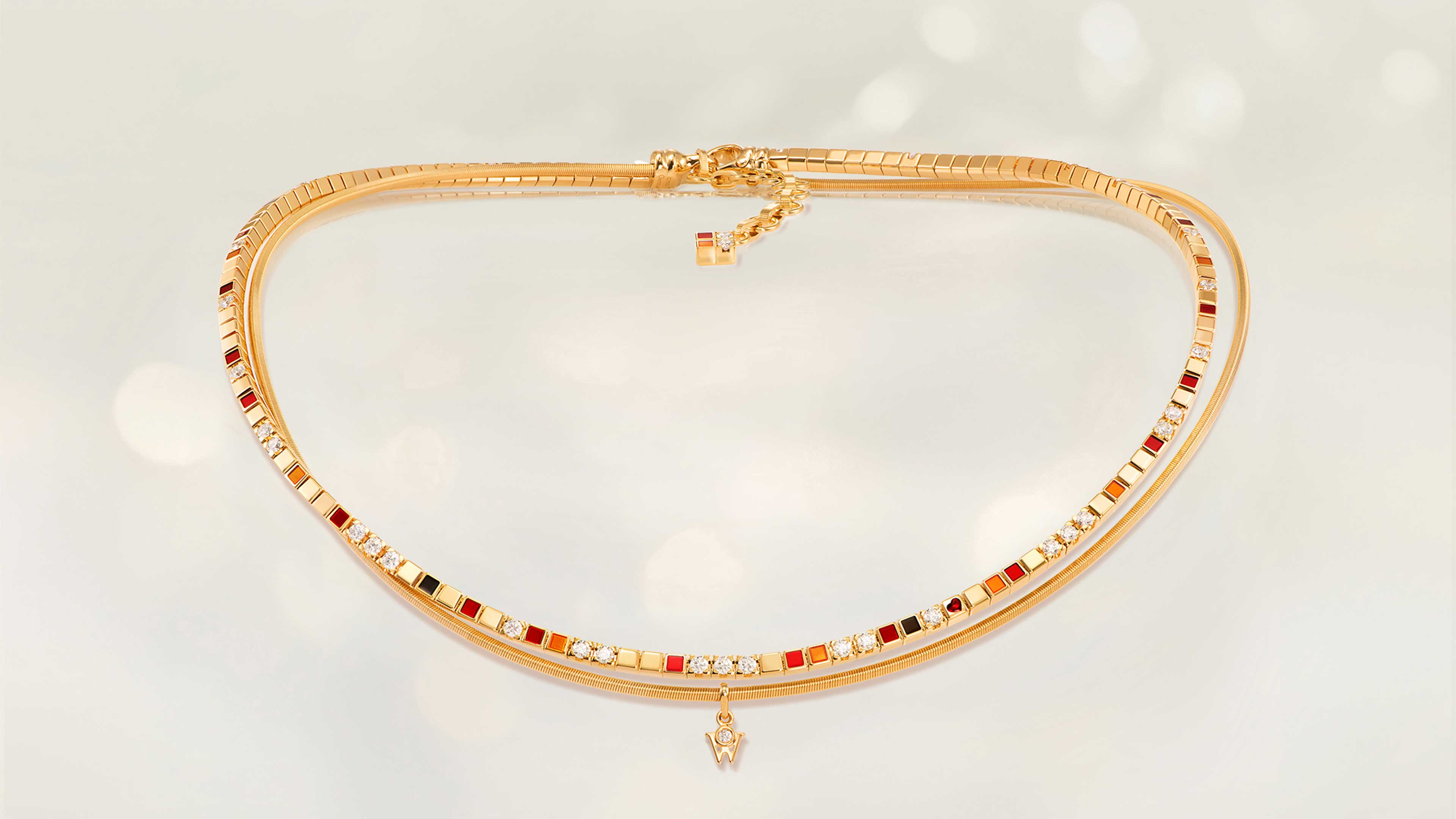 Das Collier POWER IN RED aus 18 Karat Gelbgold vereint rote, orange und schwarze Kaltemaille mit einem kleinen roten Herz. Collier auf hellem Hintergrund.