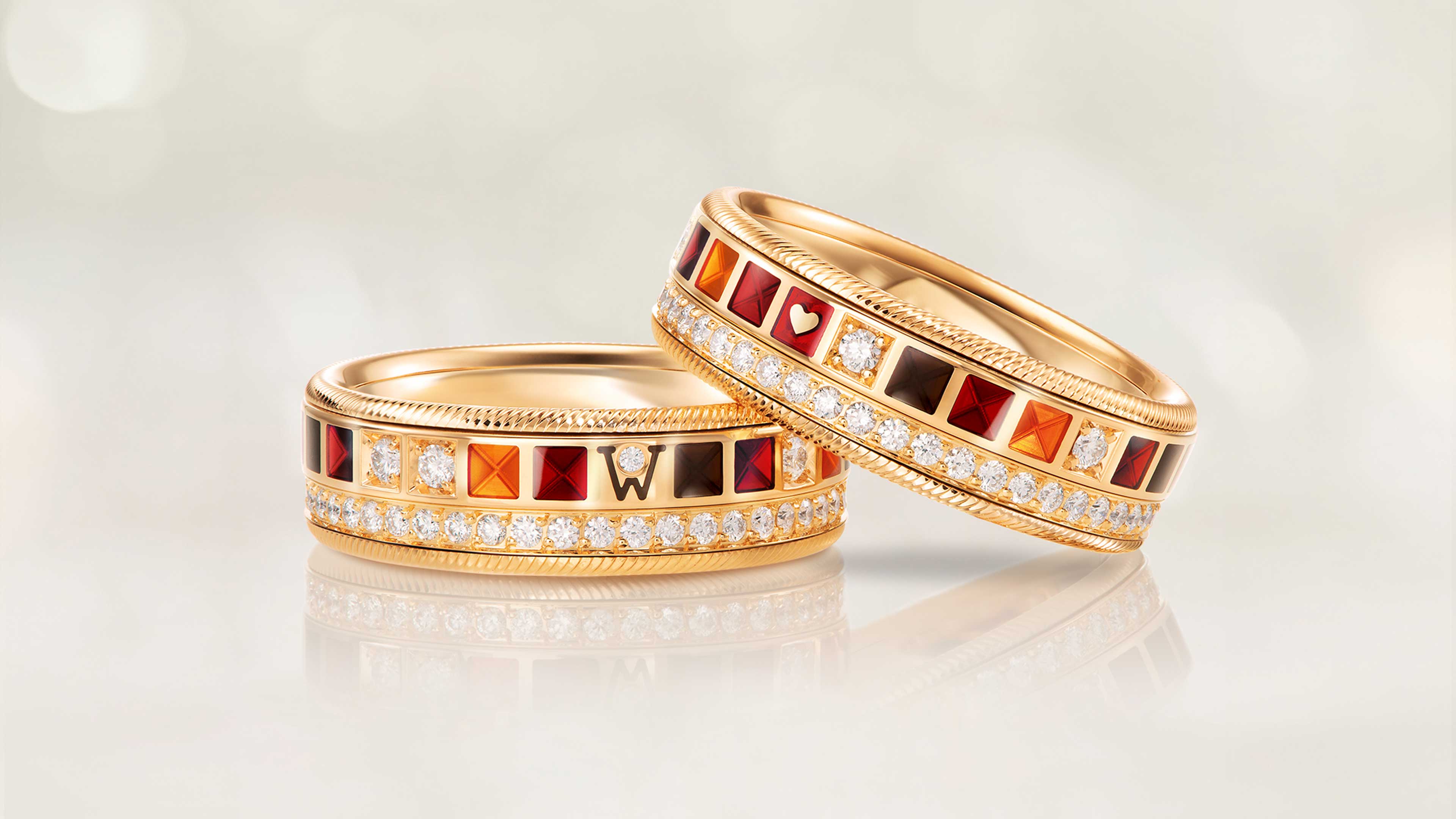 Der Ring POWER IN RED aus 18 Karat Gelbgold vereint rote, orange und schwarze Kaltemaille mit einem kleinen Herz und Brillanten auf hellem Hintergrund.