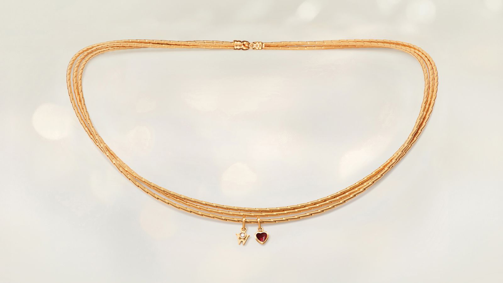Das Collier MEIN HERZ Trio aus seidenweichem 18-karätigem Gold mit einem romantischen Herz gefüllt mit Wellendorff-Kaltemaille. Auf grauem Mood Hintergrund.