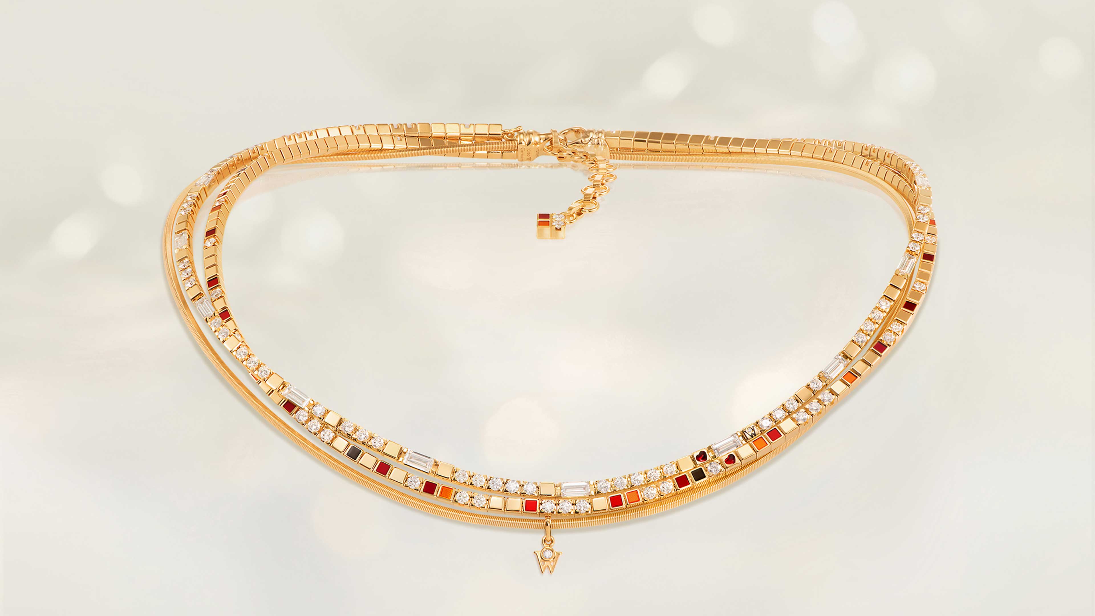 Das Collier POWER IN RED edel aus 18 Karat Gelbgold kombiniert rote, orange und schwarze Kaltemaille, Brillant-Baguettestrang und ein rotes Herz. Collier auf hellem Hintergrund.