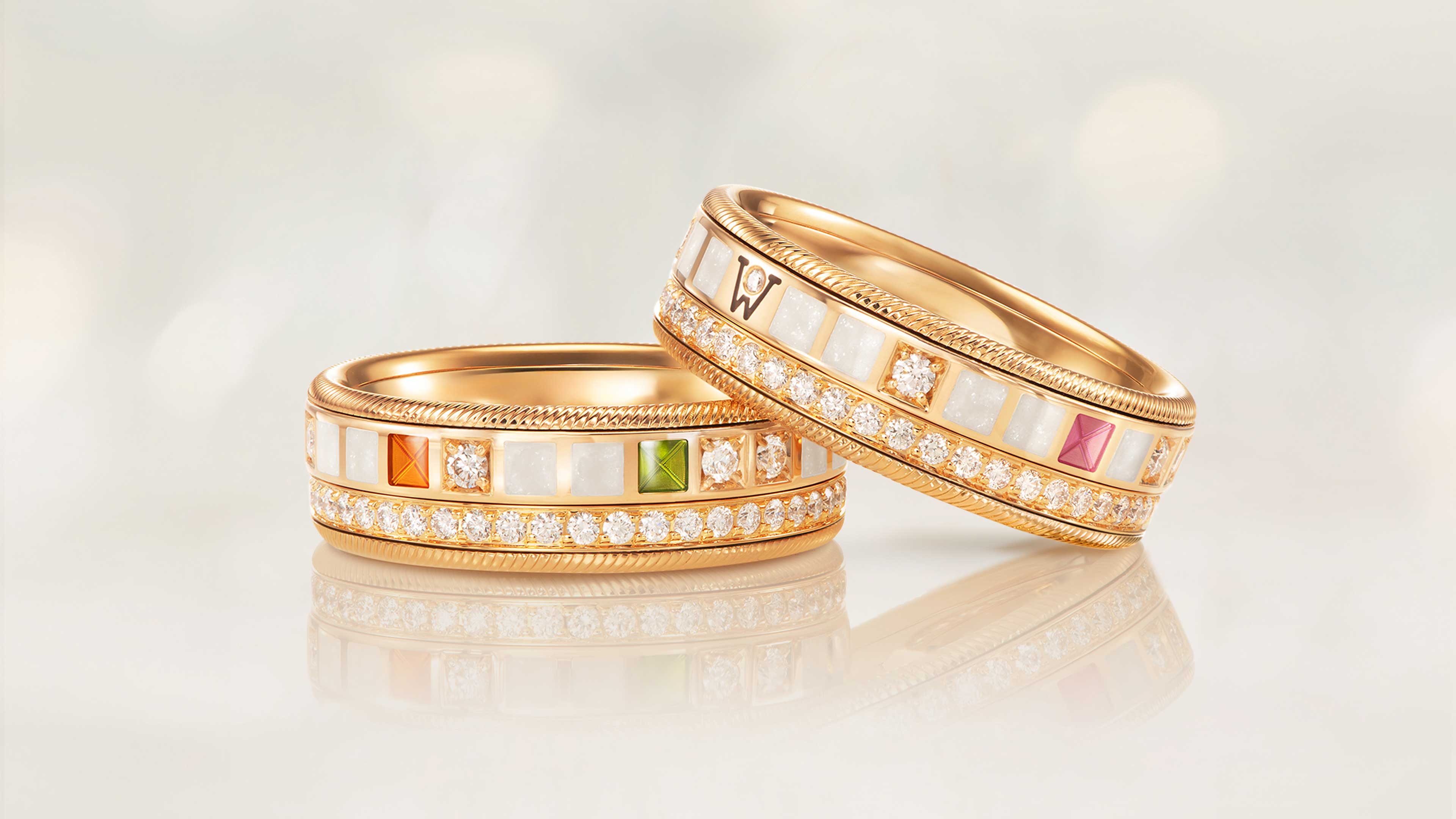 Der Ring POWER IN WHITE aus 18 Karat Gelbgold kombiniert Perlmuttweiß, Orange, Rosa, Grün, schwarze Kaltemaille, Sternenstaub und Brillanten auf hellem Hintergrund.